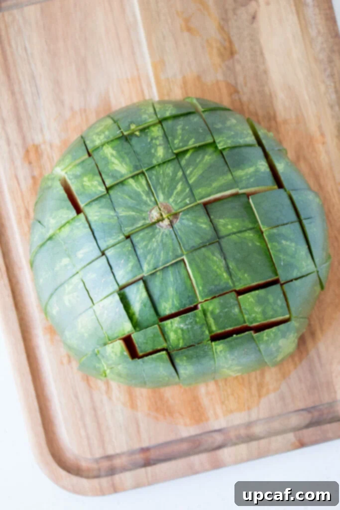 A watermelon half scored into a grid pattern, ready to be pushed into sticks.