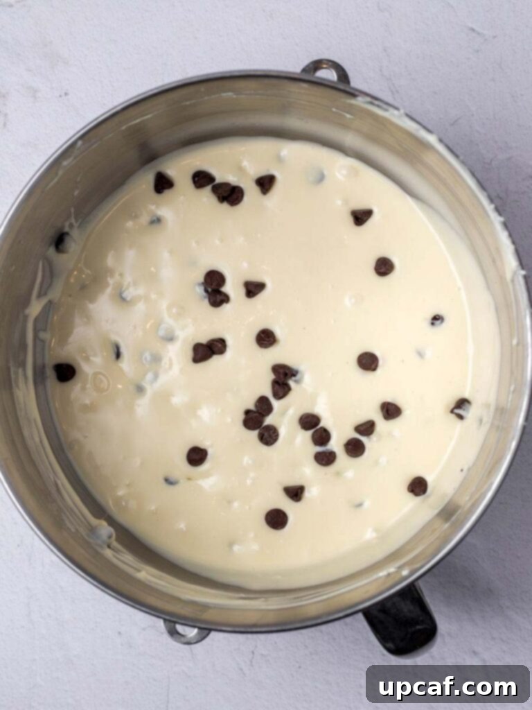Ultimate Chocolate Chip Cheesecake 4 Close-up shot of creamy chocolate chip cheesecake batter being poured over a golden graham cracker crust in a springform pan.